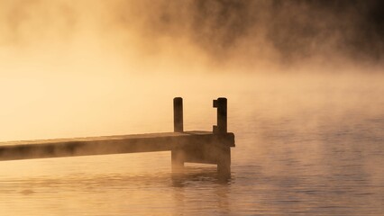 Wooden pier jutting out onto a lake, boasting a picturesque sunrise amidst a foggy atmosphere