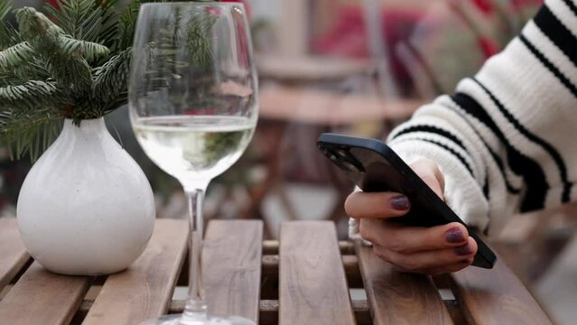 glass with sparkling wine and coffee cover on outdoor cafe table.girl taking photos,using smartphone,typing message.for christmas tree branches, happy new year.
