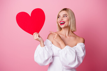 Photo of sweet impressed girl dressed white outfit pointing looking red heart empty space isolated pink color background