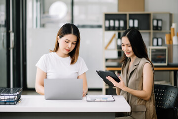 Two Asian businesswoman discuss investment project working and planning strategy with tablet laptop computer