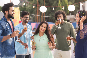 Groups of youthful friends with wine glasses in hand dancing together during birthday evening party - concept of festive celebration, entertainment and gathering