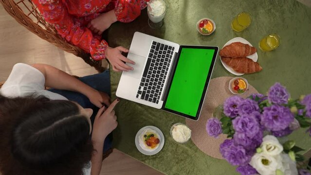 In the picture on top sit in the cafe girls, girlfriends. On the table dessert and drinks. Portray a friendly meeting they look into an outdoor laptop with green screen. Place for advertising