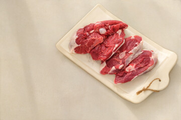 Lamb meat on a ceramic board on beige background. Meat for cooking. Rear part of the meat carcass. Top view.