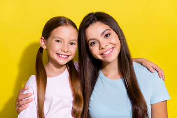 Photo of good mood charming little sisters wear t-shirts embracing smiling isolated yellow color background
