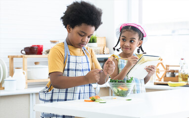 African siblings, boy in apron cooking, making mixing salad in bowl with little girl wear chef hat,...