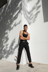 Full length of confident and muscular young cuban man in eyeglasses and trendy outfit crossing arms