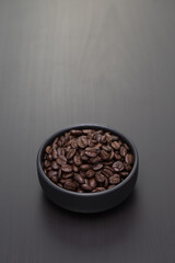 Dark roasted coffee beans in a small black ceramic bowl.