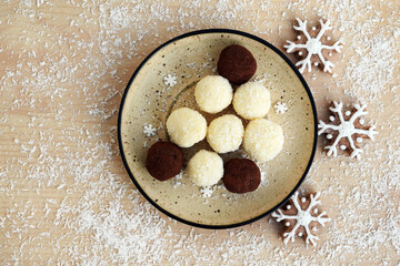 Plate with unbaked coconut balls and chocolate truffles, on background with shredded coconut and...