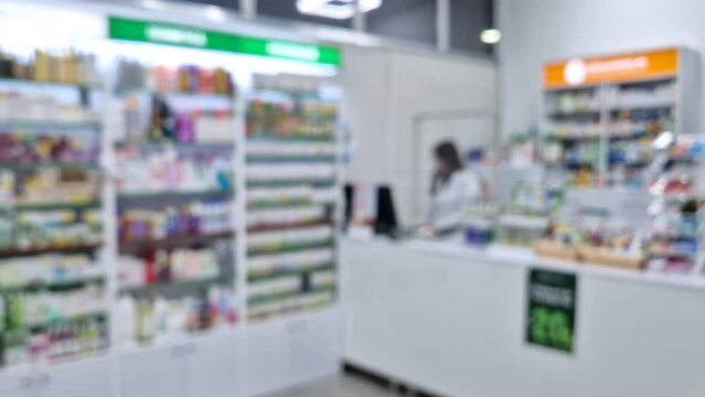 Blurred view inside of pharmacy with female pharmacist at workplace around stocked shelves with medicine. Healthcare and cosmetics industry defocused background