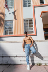 Sexy cuban man with athletic body in baseball cap and jeans standing on street in Miami