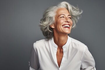 A woman with grey hair is pictured smiling while wearing a white shirt. 