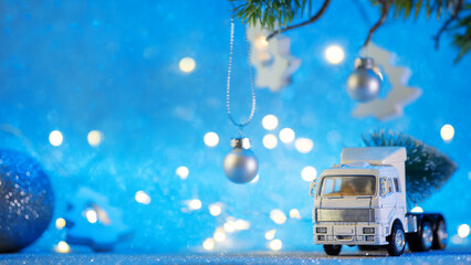 A toy truck is transporting a Christmas tree. Blue shiny background, a branch of a Christmas tree...