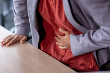 Stomach ache, sick business woman holding hands on stomach close up, female worker at workplace working at table with laptop inside office - obrazy, fototapety, plakaty