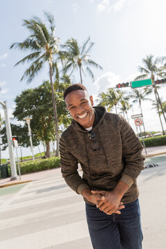 happy african american man in hoodie smiling while standing near palm trees in Miami