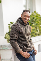 smiling african american man in hoodie holding stylish sunglasses while standing outdoors