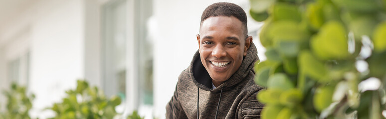 happy african american man in hooded sweatshirt looking at camera outdoors, banner