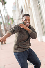 excited african american man in wireless earphone listening music and dancing on street in Miami