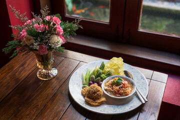 Crisp Catfish Flake Salad in white plate with bouquet of flowers in a vase on wooden table. Thai appetizer healthy dish beside with mix of vegetables and sauces. Thai Food.