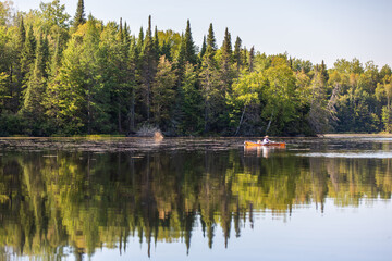 A man fly fishing from a kayak on a calm Northwoods Wisconsin lake with a pine forest behind him.
