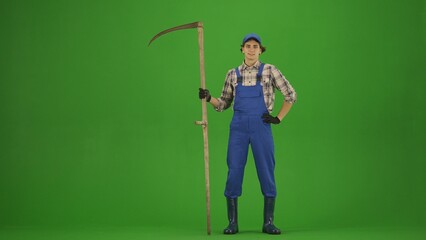 Portrait of farmer in working clothing on chroma key green screen. Gardener standing posing at the camera with old scythe.