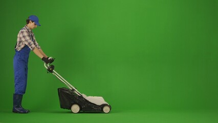 Portrait of farmer in working clothing on chroma key green screen. Gardener standing and mowing the grass with petrol lawn mower.