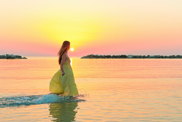 Fototapeta na wymiar Beautiful young woman running on water in a yellow dress early in the morning at sunrise