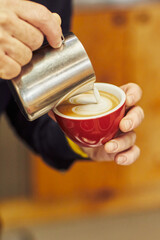 Close-up of a barista pouring milk into a red cup to create latte art.