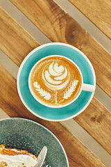 Aerial view of a cappuccino with intricate leaf latte art in a teal cup, on a wooden table