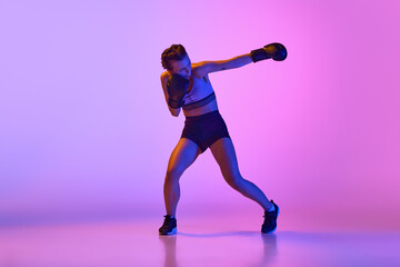 Fototapeta na wymiar Dynamic and intense, female professional boxer showcases her athleticism against gradient violet studio background in neon light.