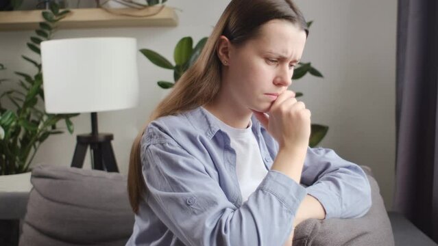 Close up of anxious tired young caucasian woman sitting on couch, feeling doubtful making difficult decision. Nervous unhappy lady 25s suffering from negative thoughts, relationship problems concept