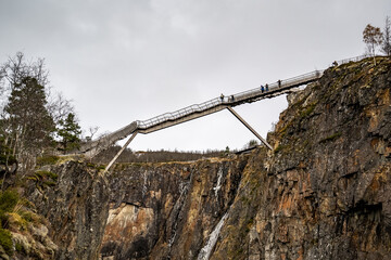view of metal bridge over Vøringfossen waterfall with tourists on it in norway