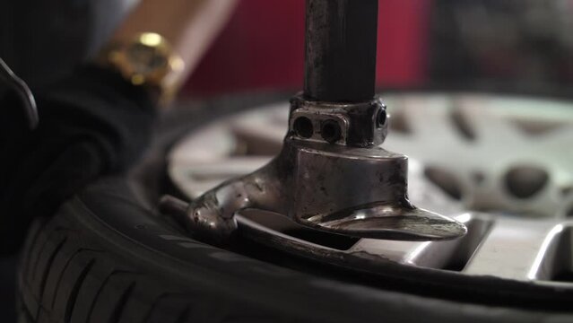 Repairman clamp wheel disk in fitting machine to remove rubber tire.