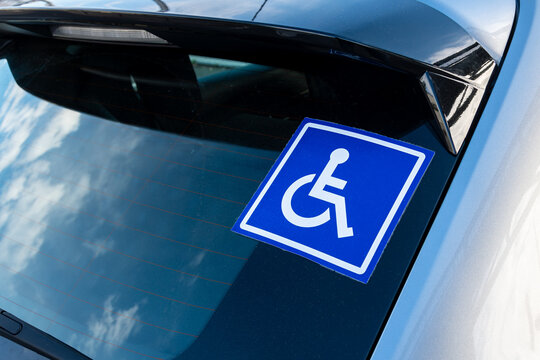 Autocollant bleu sur la vitre arri&egrave;re d'une voiture avec un pictogramme blanc repr&eacute;sentant une personne en situation de handicap en fauteuil roulant
