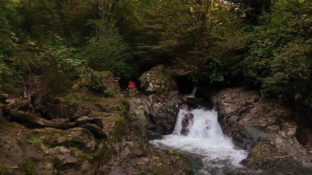 Man is waking near amazing cascade in Mingrelia forest with water flowing from rock surrounded by trees and plants filmed in slowmo. Male tourist is trekking in Georgia woodland. Union with nature