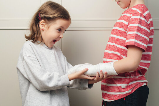 Boy broken arm, girl is in shock. Child girl holding his brother's broken arm. Boy holds hand bent broken arm cast on his arm