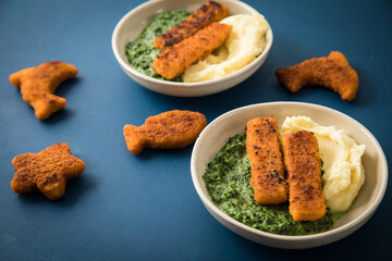 Gebratene Fischstäbchen und Figuren als Fisch, Seestern und Delfin für Kinder mit Rahmspinat und Kartoffel Püree in Schale mit dunkel blau Hintergrund © Christin Klose