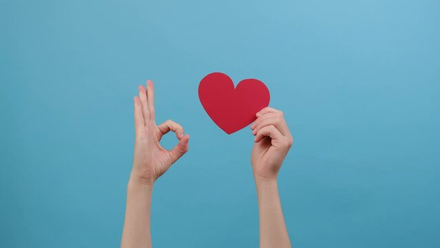 Close up of female blogger holding in hands little red heart, showing ok sign, isolated on blue background. Like blogging blog social network tenderness concept. Valentine's day international women