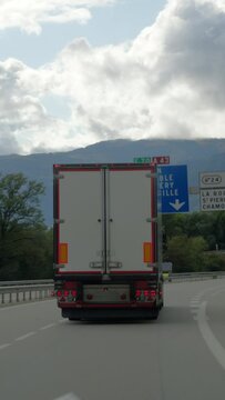 Vertical video - a rear view of a large truck traveling on a highway with a picturesque mountain backdrop and cloudy skies overhead