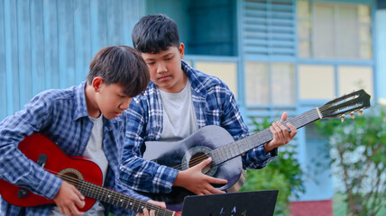Young Asian boys are playing acoustic guitars in front of a house, soft and selective focus        ...