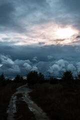 Dramatic cloudy sky at dusk with a glimpse of warm light over a rugged countryside path, hinting at the calm before the storm and the majestic play of light and shadow on a rural road.