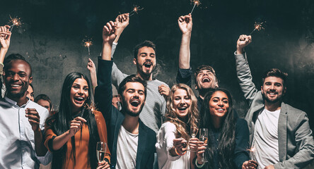 Group of happy young friends holding champagne flutes and sparklers while having fun in night club...