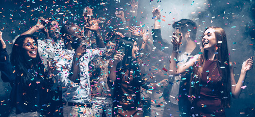 Group of happy young friends dancing and enjoying celebration in night club while confetti flying around