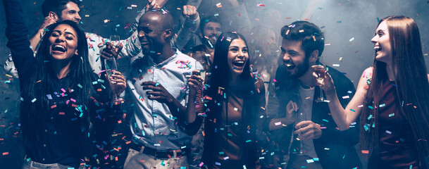 Happy young people dancing and celebrating New Year in night club while confetti flying around