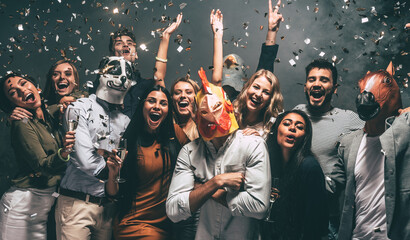 Group of happy young people in animal masks enjoying celebration in night club with confetti flying...