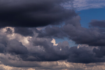 Epic storm dark grey black and white cumulus rainy clouds against blue sky background texture, thunderstorm