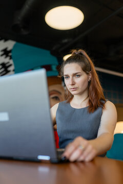 Confident concentrated businesswoman with high ponytail works on impotant project. Brunette lady works on laptop in lounge room