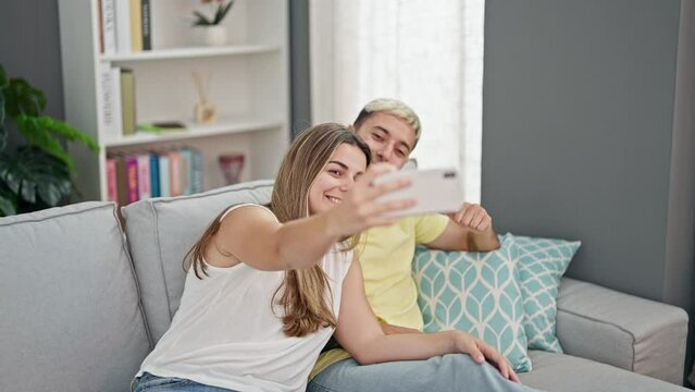 Beautiful couple taking selfie picture with smartphone sitting on the sofa at home