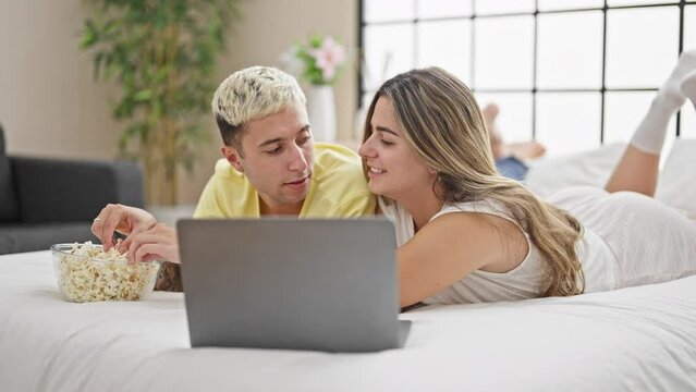 Beautiful couple watching movie on laptop eating popcorn at bedroom
