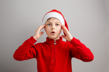 Cheerful boy in Santa hat on isolated gray background showing different funny emotions, surprise, joy, delight.