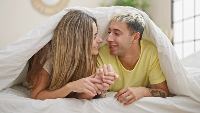 Beautiful couple lying on bed covering with blanket kissing at bedroom